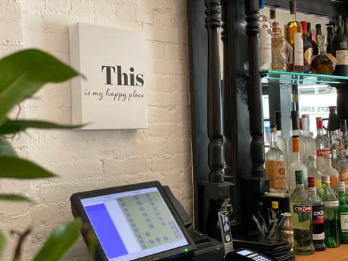 A wall sign reading "This is my happy place" above the bar register and bottles