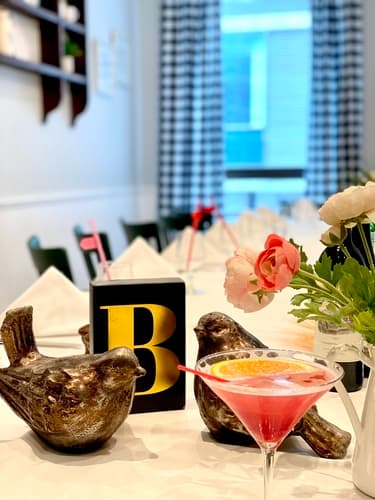 A pink cocktail beside two bronze bird figures and flowers on a table