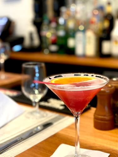 A pink cocktail in a coupe glass on the bar