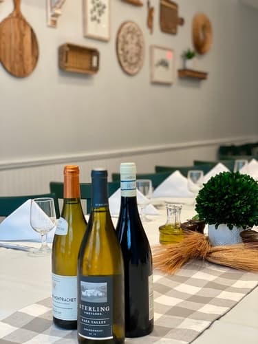 Three bottles of white wine on a gingham table runner beside a potted boxwood