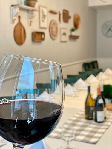 A glass of red wine on a table in the dining room with wine bottles behind it