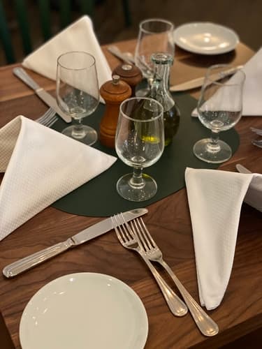 A place setting with a folded napkin, wine glasses and silverware on a wood table