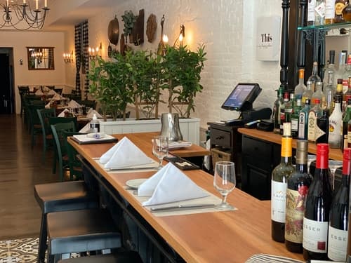 The bar with a wood counter and bottles on the back shelf, the dining room beyond