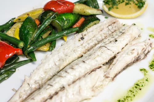 Grilled fish with roasted peppers, green beans and a lemon wedge