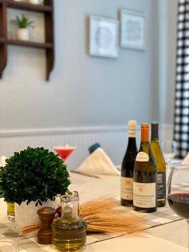 A table set with wine bottles, olive oil and a cocktail beside a potted boxwood