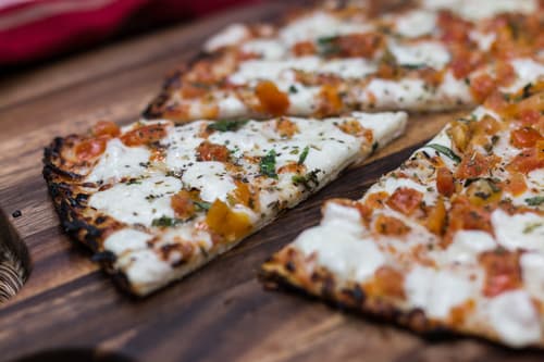 Flatbread topped with tomato and cheese on a wooden board