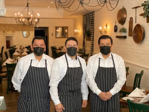 Three servers in striped aprons and masks standing in the dining room