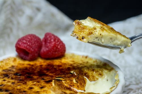 Creme brulee topped with raspberries, a spoonful lifted from the dish