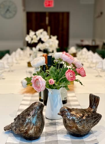 Two bronze bird figures and a vase of flowers on a long table set for an event