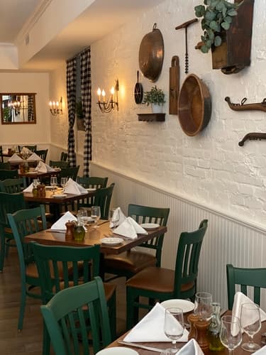 Wood tables set with napkins and glasses along a white brick wall
