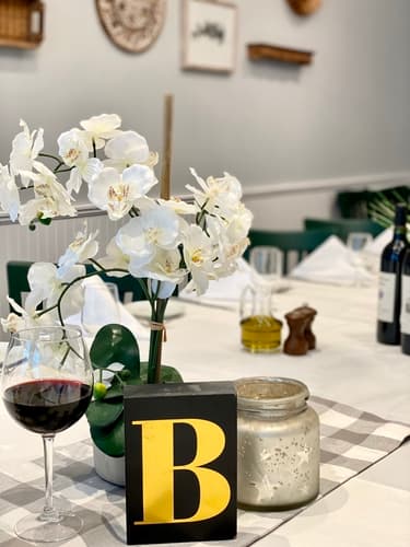 White orchids and a glass of red wine on a table with a gold letter B sign