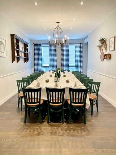 A private dining room with a long table, green chairs and a chandelier
